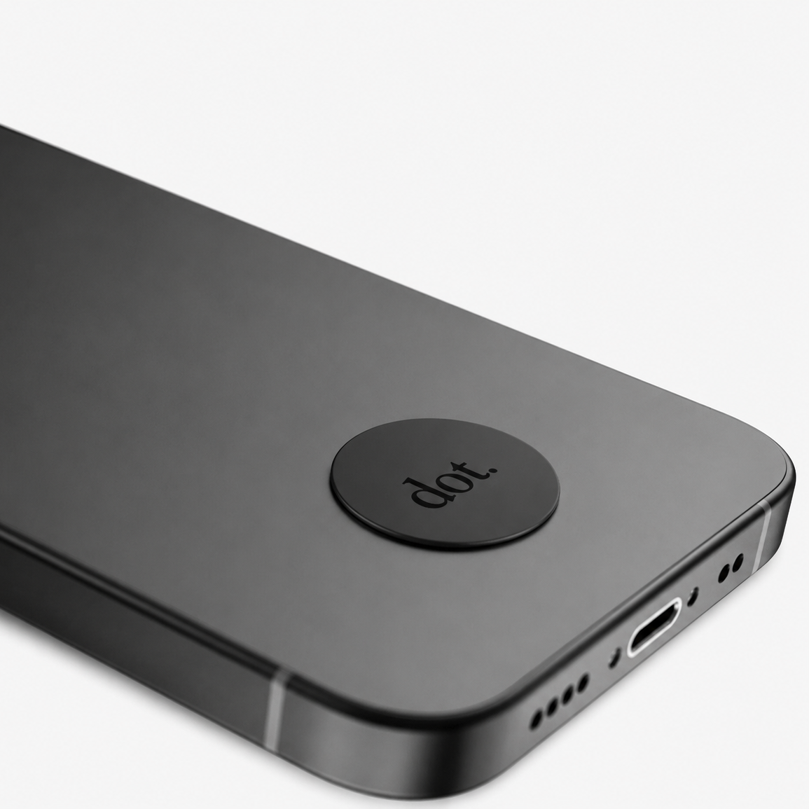 Close-up of a black smartphone showing the back corner with a circular black dot logo and a USB-C port on a light gray background.